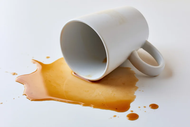 White ceramic coffee mug lying on its side with spilled coffee on a plain white surface