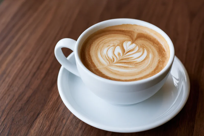 White ceramic cup with latte art rosette on wooden table