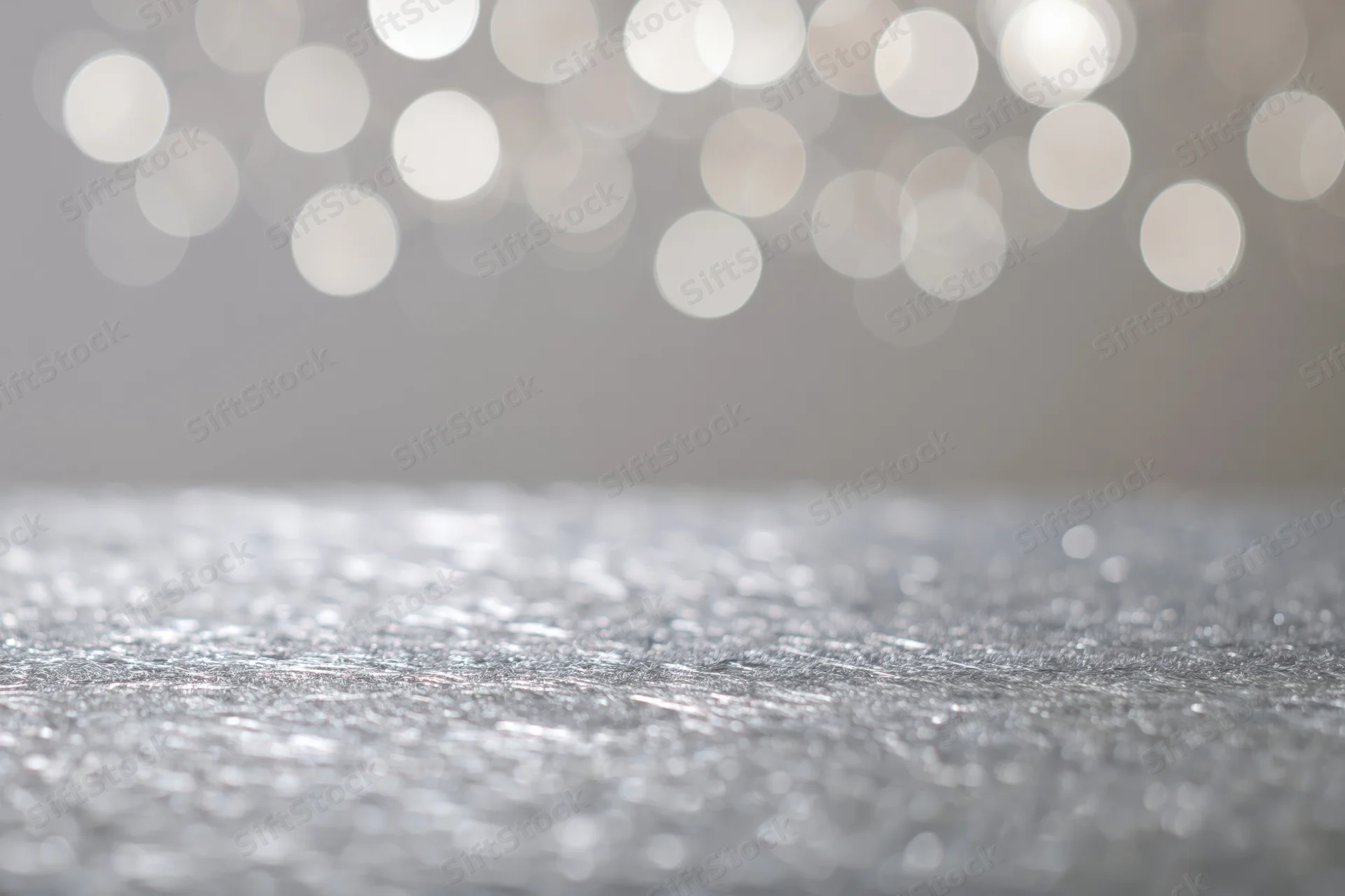 Silver glitter surface with white bokeh lights in background