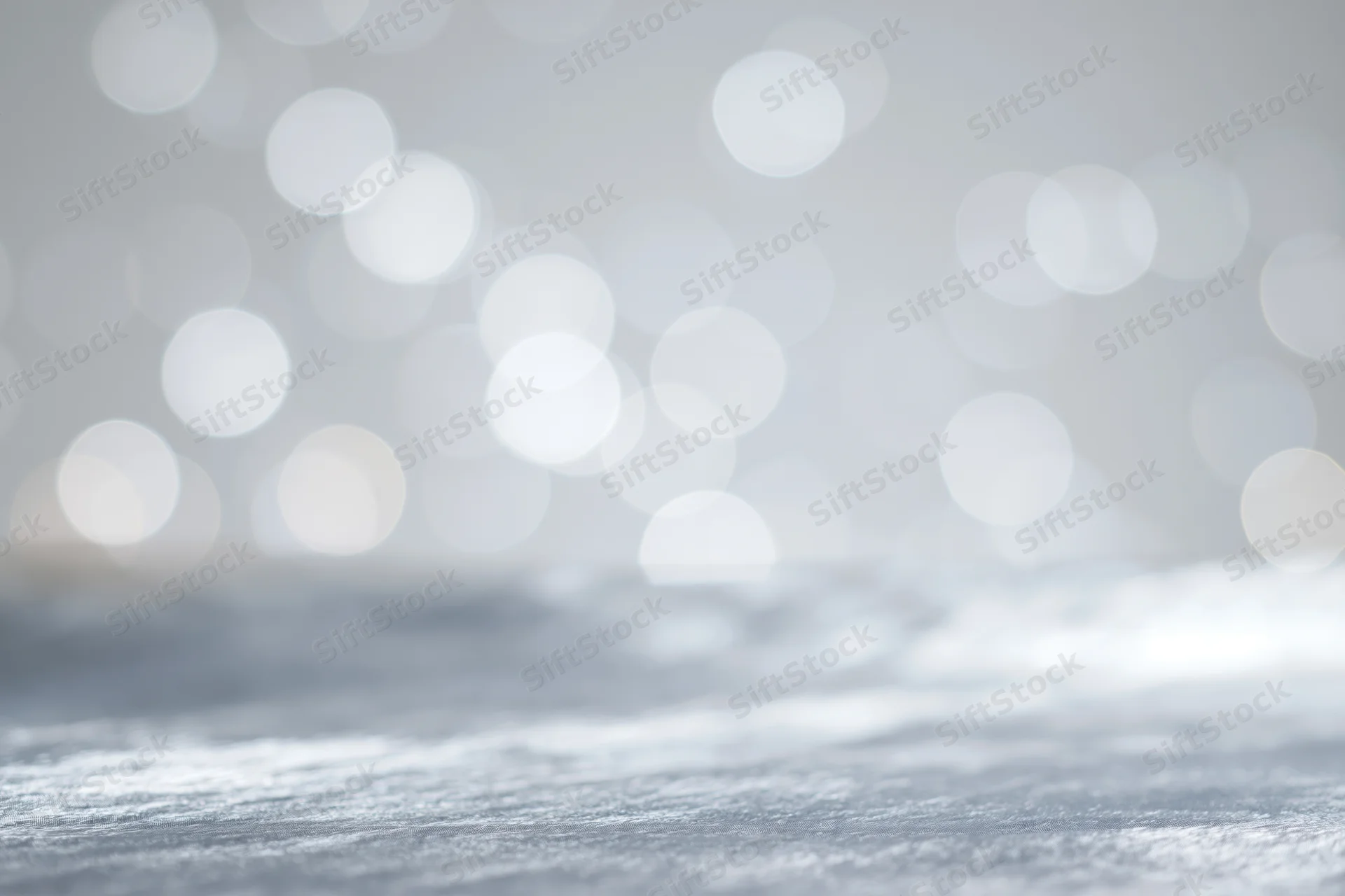 Abstract white and silver bokeh lights over a blurred reflective surface