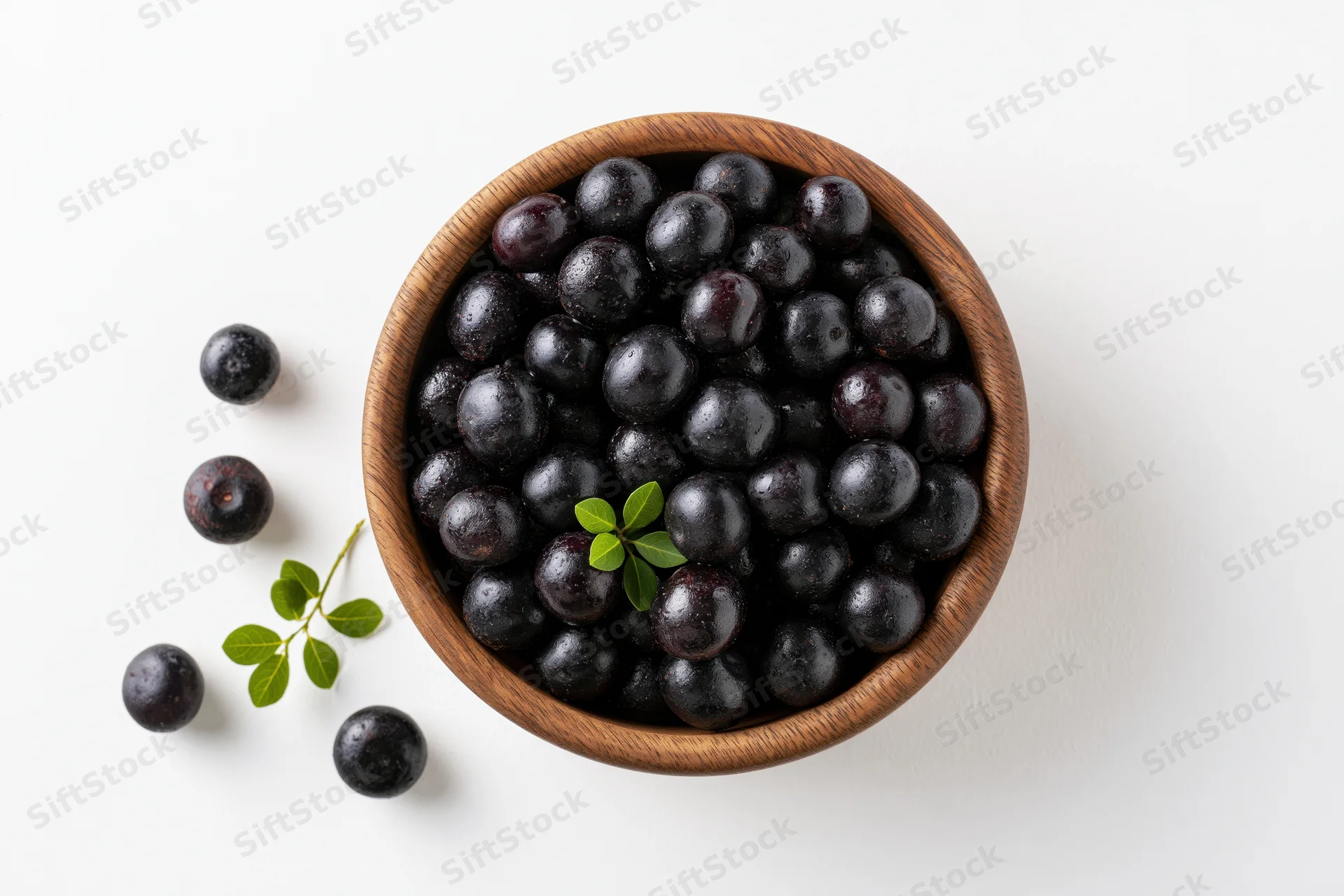 Acai berries in a wooden bowl with scattered berries and green leaves on white background