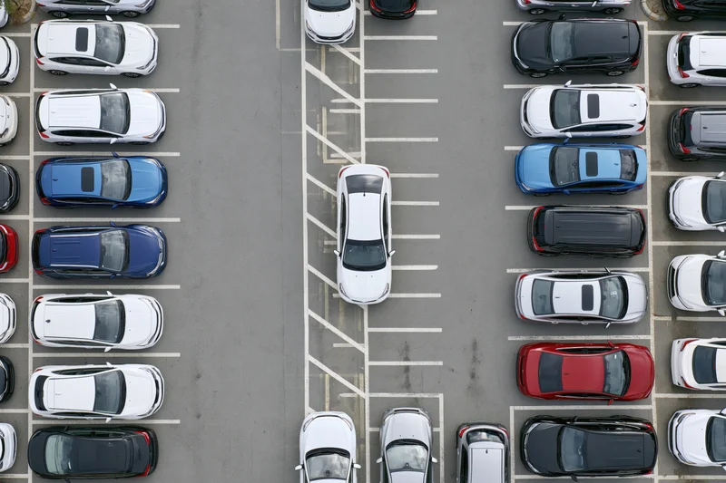 Aerial top-down view of a busy parking lot with one white car parked in a marked space among other vehicles