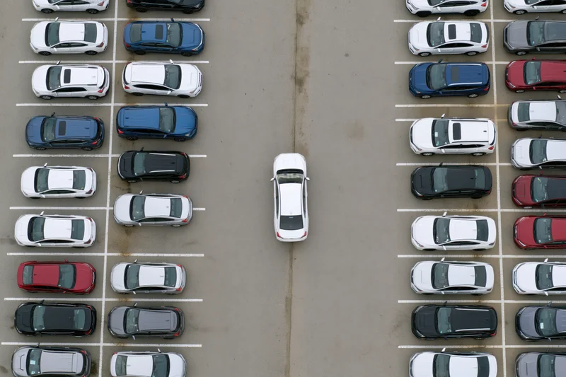Aerial top-down view of a parking lot with rows of cars and one white car in the center aisle