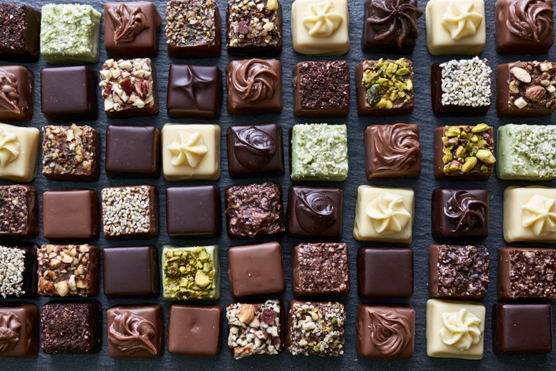 Assorted artisan chocolates and pralines arranged in neat rows on dark surface