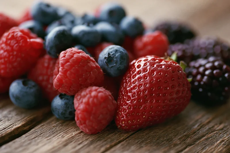 Assorted fresh berries including strawberry, raspberry, blueberry and blackberry arranged on a wooden surface