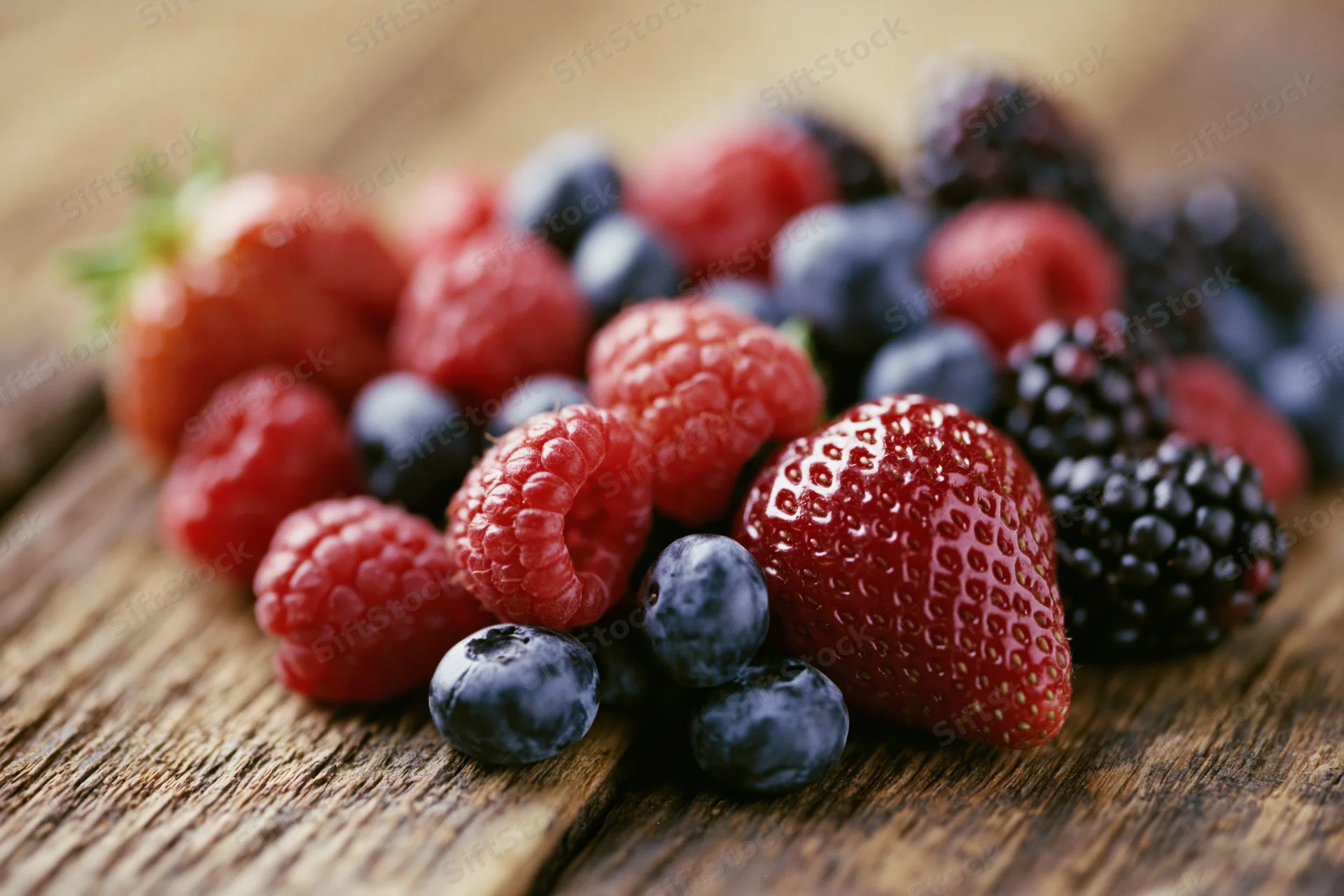 Assorted fresh berries including strawberry, raspberry, blueberry and blackberry arranged on a wooden surface