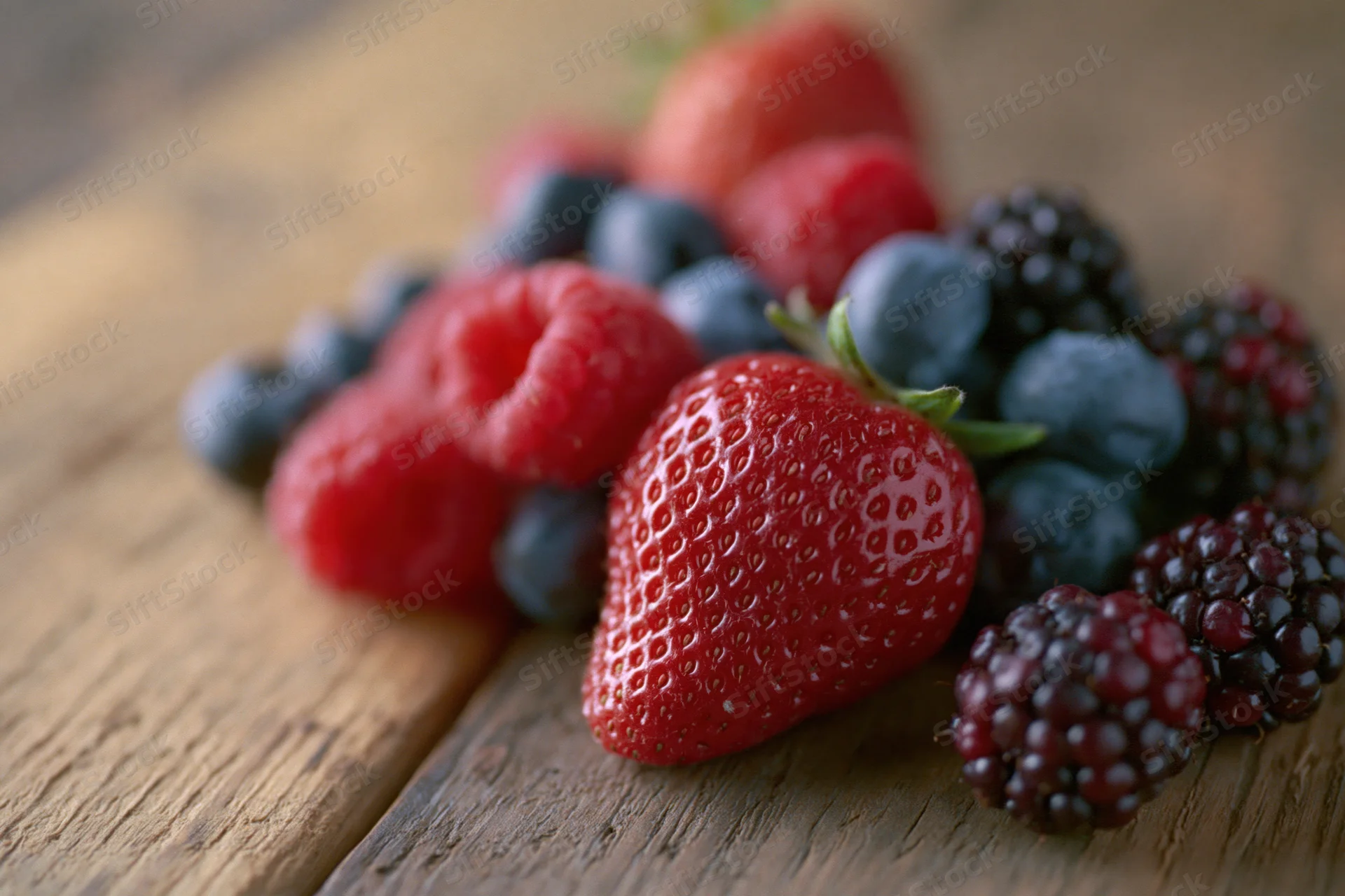 Assorted fresh berries including strawberry, raspberry, blueberry and blackberry arranged on a wooden surface