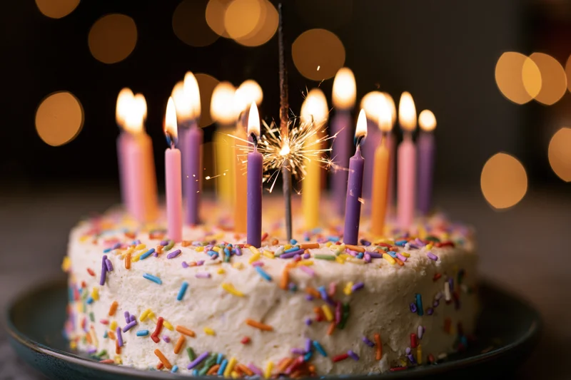 Birthday cake with lit candles and sparkler on plate against bokeh lights