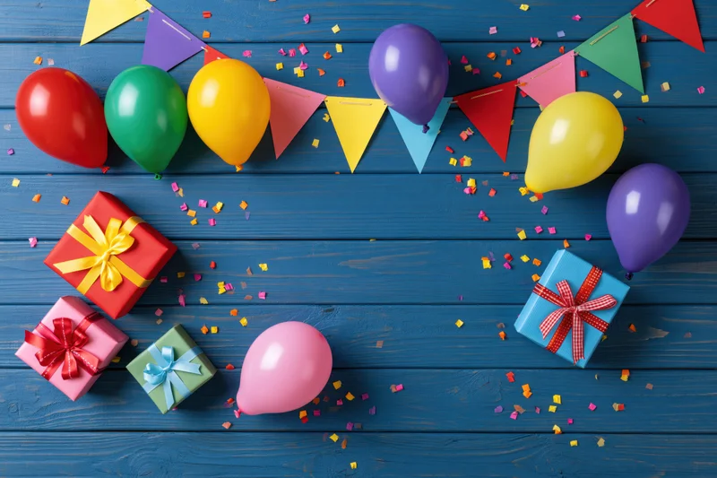 Colorful birthday party decorations and gifts arranged on blue wooden surface with confetti and bunting