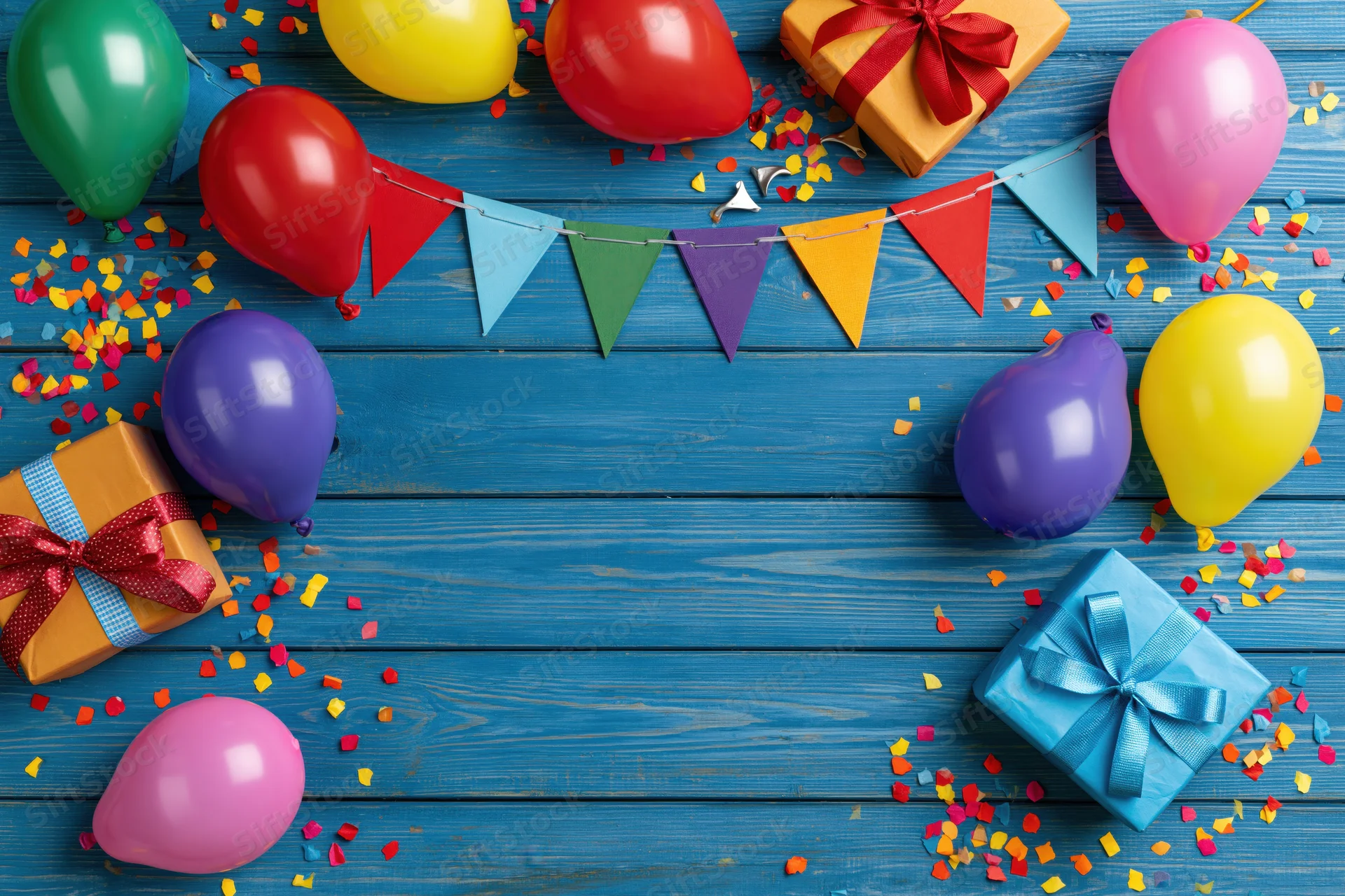 Colorful birthday party decorations and gifts arranged on blue wooden surface with copyspace in center