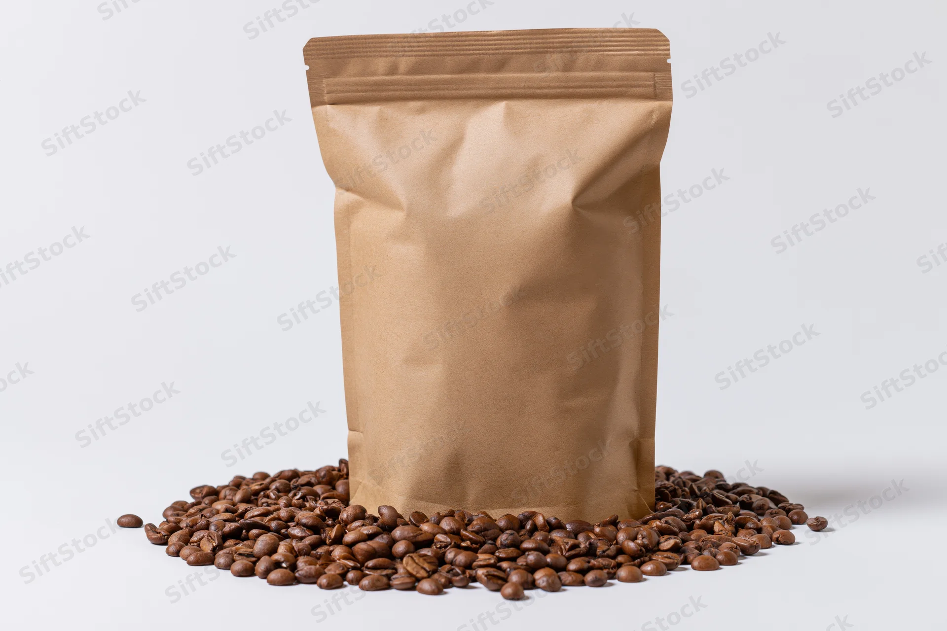 Brown kraft paper coffee bag standing upright with roasted coffee beans scattered around on white background