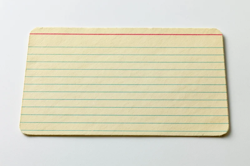 Vintage blank index card with green lines and red top line lying flat on white surface