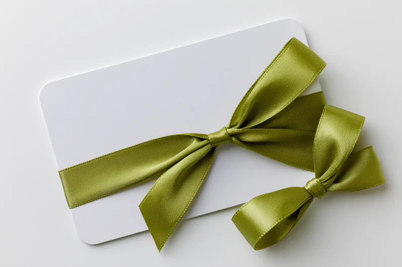 White gift card with olive satin ribbon tied in bow on plain surface