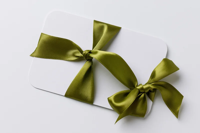 White gift card with olive satin ribbon tied in bow on plain background