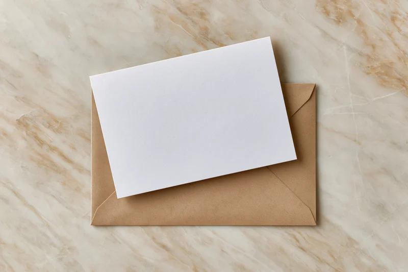 Blank white card resting on a brown envelope on a marble surface