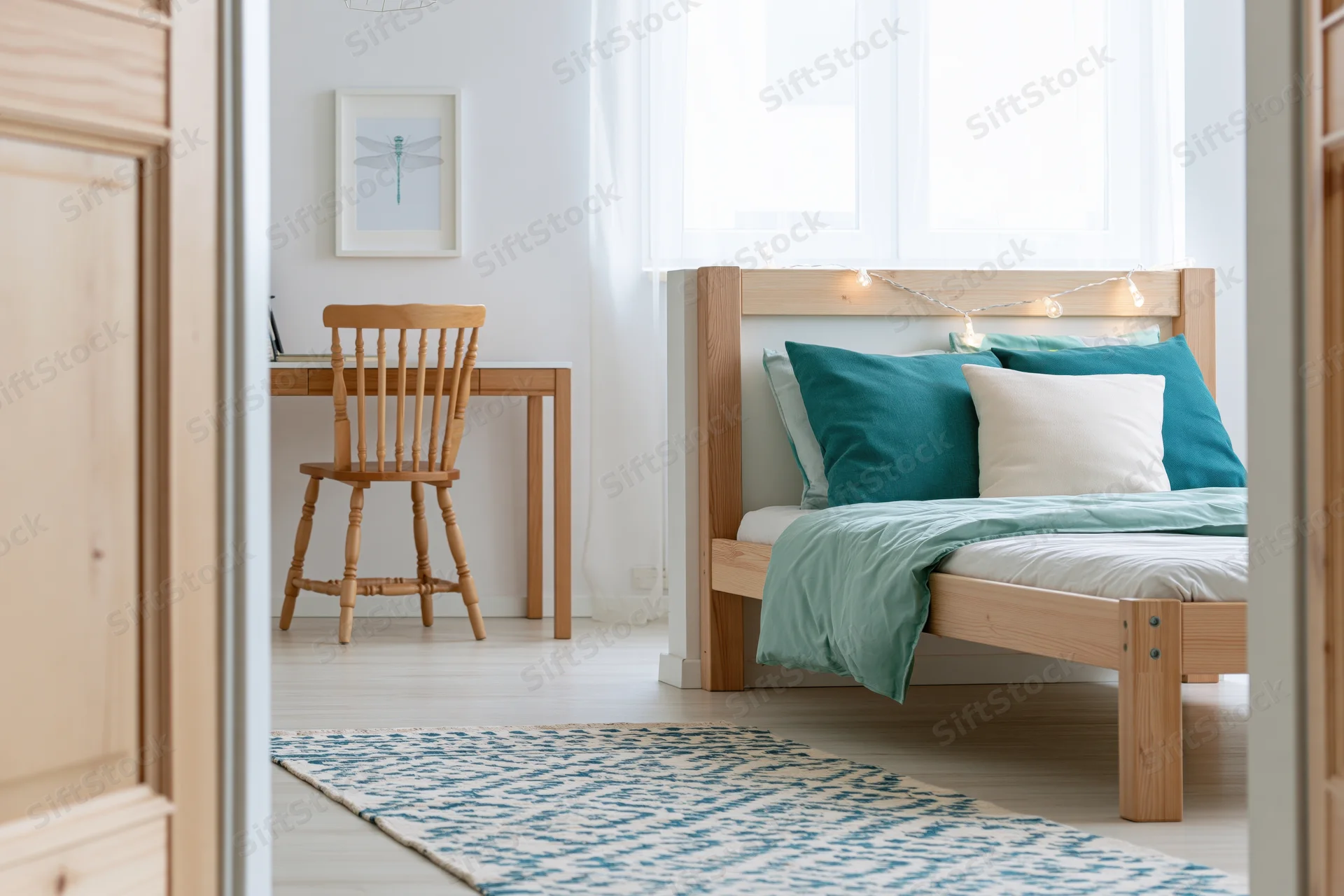 View into a bright minimalist child's bedroom with wooden bed and desk through an open door