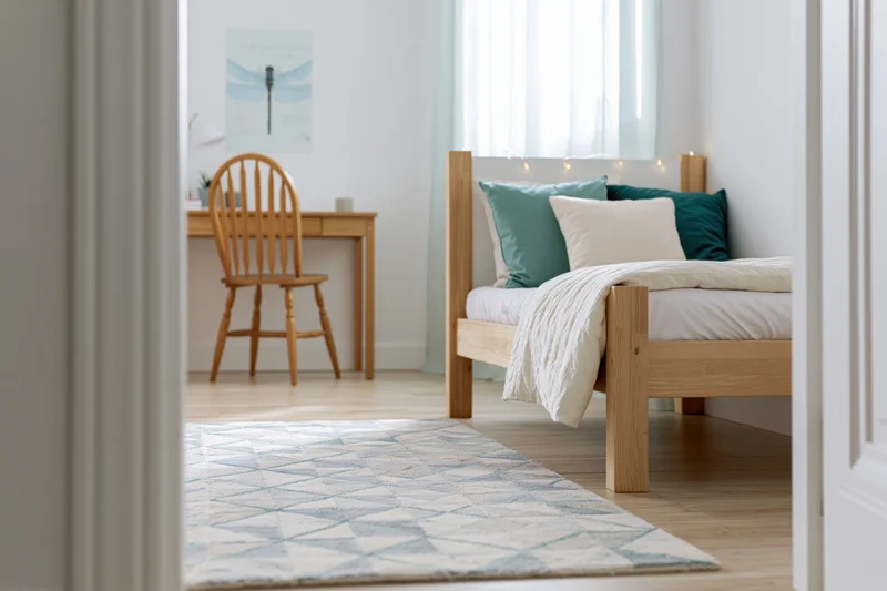 View into a minimalist child's bedroom with wooden bed and desk through an open door