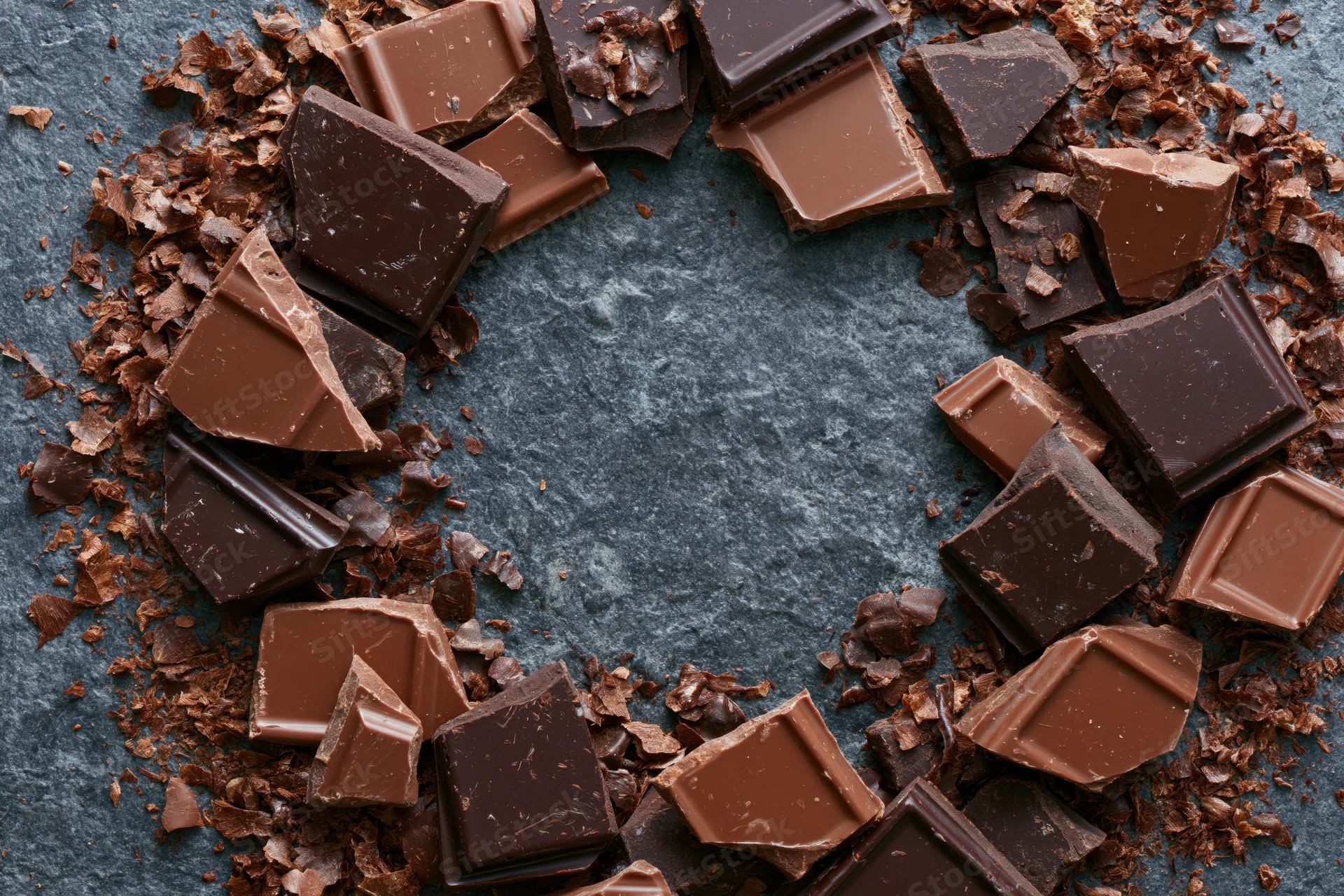 Broken dark and milk chocolate pieces arranged in a heart shape on a slate surface with central copyspace