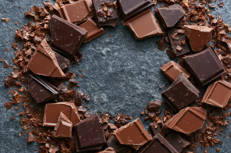 Broken dark and milk chocolate pieces arranged in a heart shape on a slate surface with central copyspace