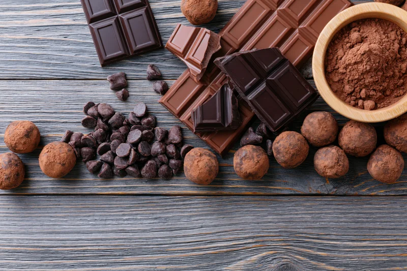 Dark and milk chocolate bars broken and scattered with chocolate chips and cocoa powder on a rustic wooden table