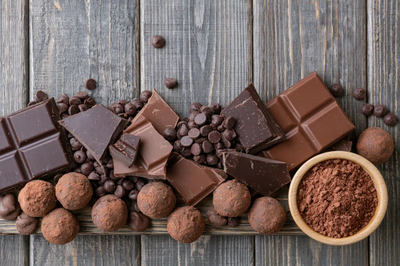 Broken dark and milk chocolate bars scattered with chocolate chips and cocoa powder on a rustic wooden surface