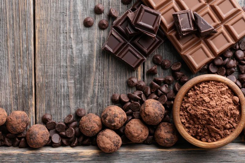 Broken dark and milk chocolate bars with chocolate chips and cocoa powder arranged on a rustic wooden table