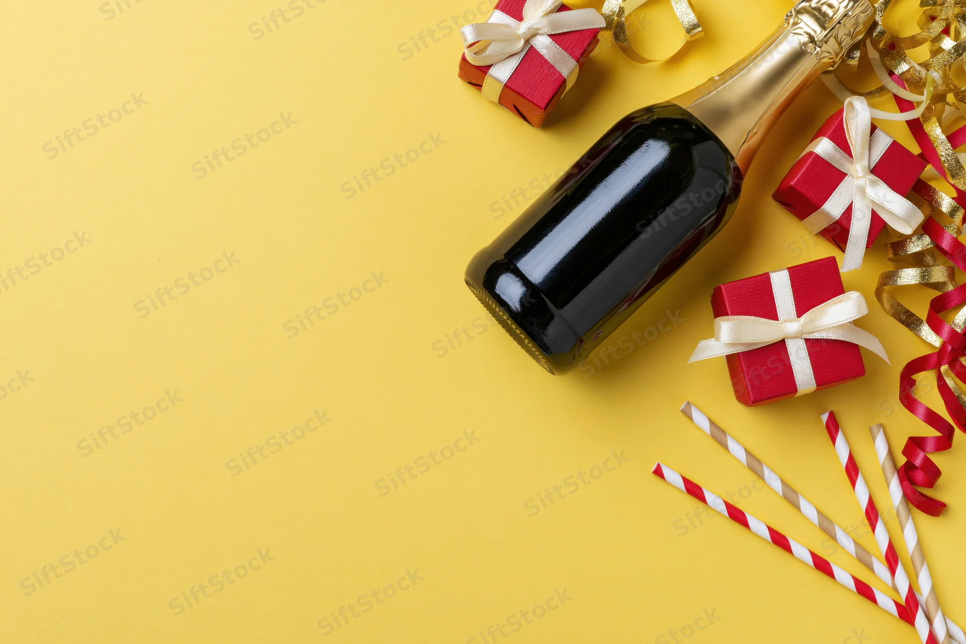 Champagne bottle lying on its side next to red gift boxes and party decorations on yellow background