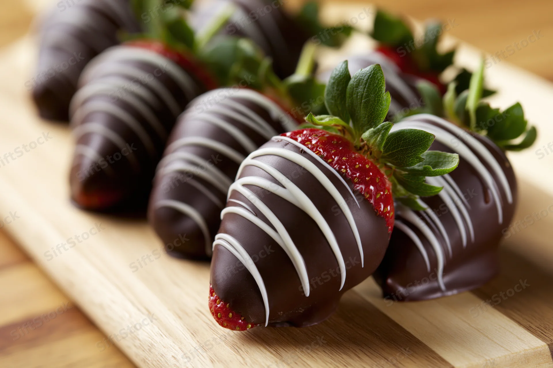 Chocolate-dipped strawberries with white chocolate drizzle arranged on a wooden cutting board