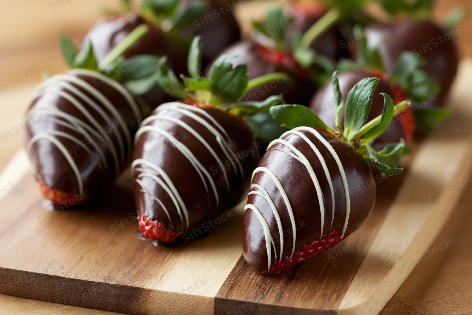Chocolate-dipped strawberries with white chocolate drizzle arranged on a wooden cutting board