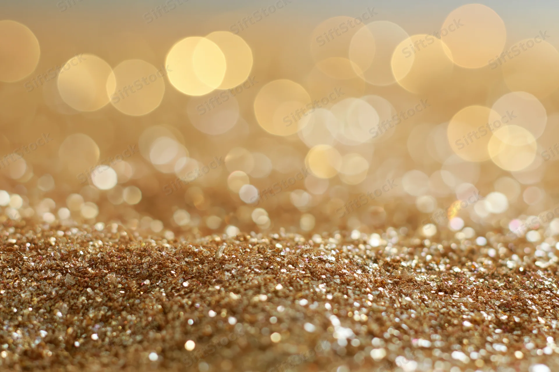 Close-up of gold glitter surface with bokeh lights in background