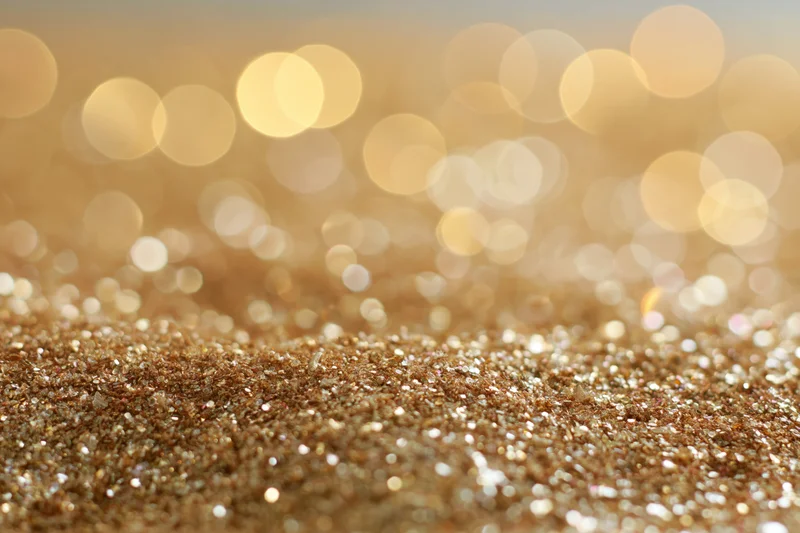 Close-up of gold glitter surface with bokeh lights in background