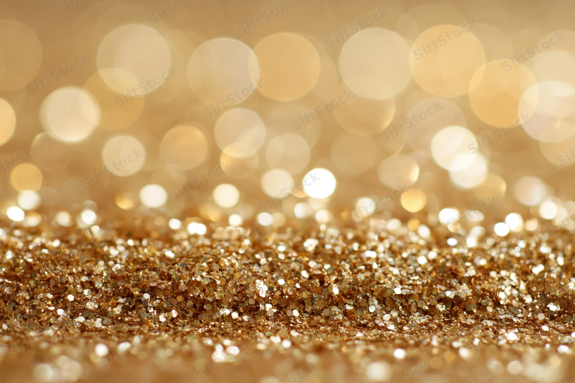 Close-up of gold glitter surface with bokeh lights in background