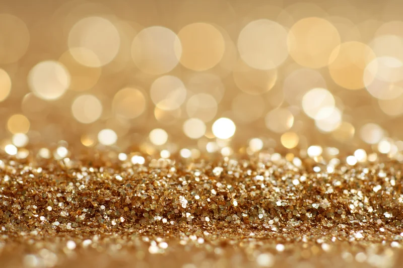 Close-up of gold glitter surface with bokeh lights in background