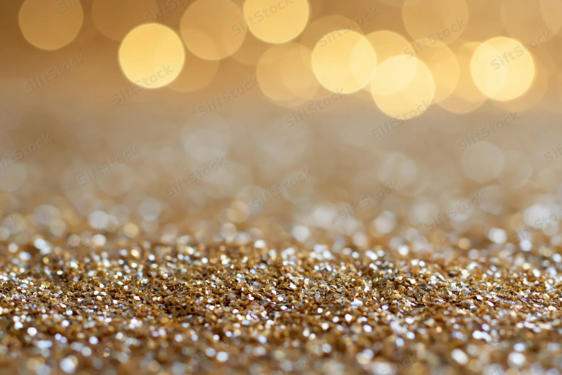 Close-up of gold glitter surface with blurred bokeh lights in background