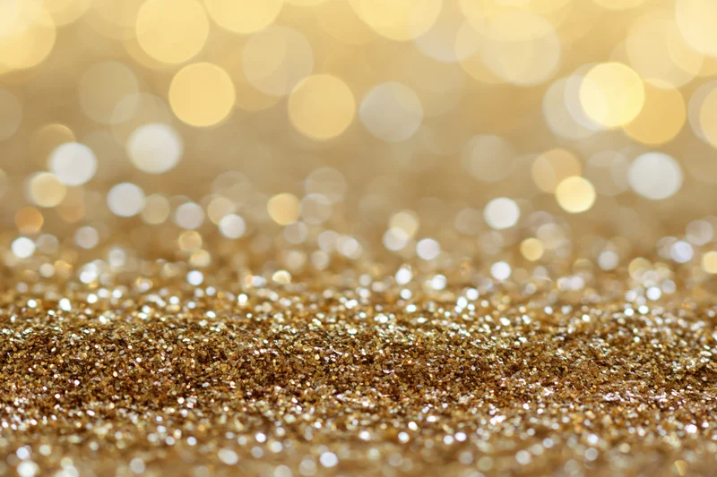Close-up of gold glitter surface with bokeh lights in background