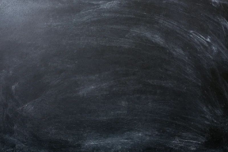 Close-up of a blank black chalkboard surface with smudged white chalk marks and erased residue, filling the frame