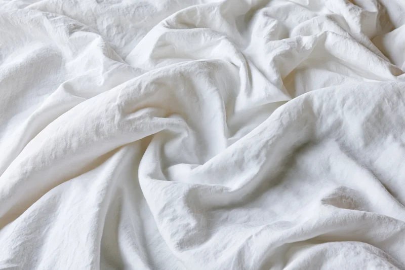 Crumpled white cotton bed sheet in close-up flat lay view