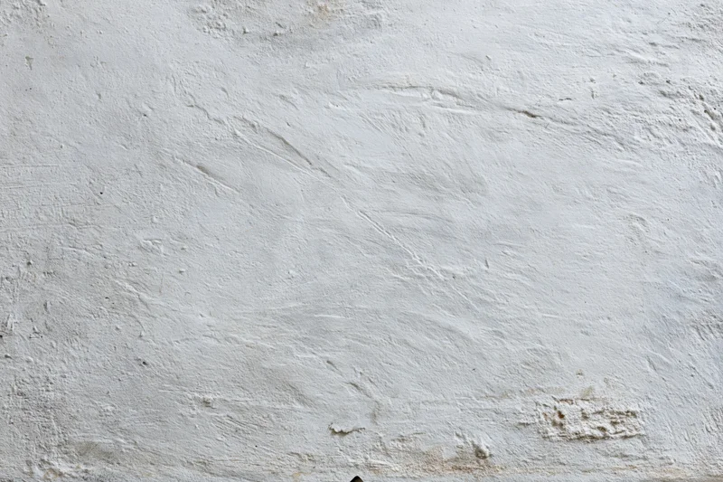 Close-up of a weathered white concrete wall surface with cracks and stains