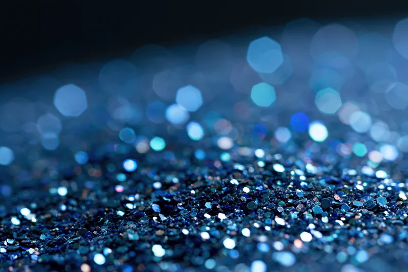 Close-up of blue glitter surface with scattered light reflections and bokeh effect in the background
