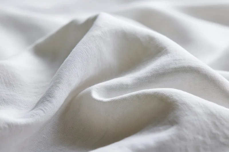 Close-up of crumpled white cotton bed sheet with soft folds and natural texture