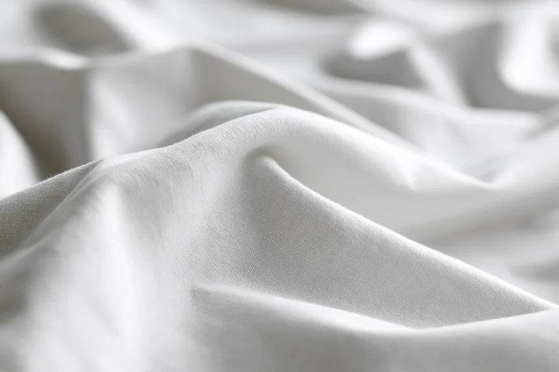 Close-up of crumpled white cotton bed sheet with soft folds and natural texture