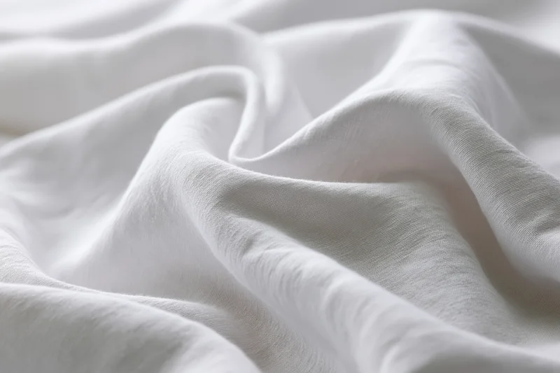 Close-up of crumpled white cotton bed sheet with soft folds and natural texture