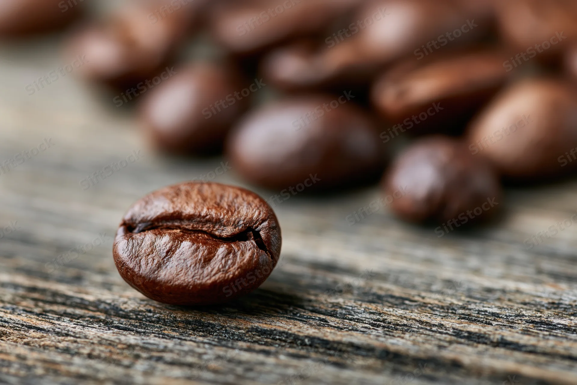 Roasted coffee bean in focus on a weathered wooden surface with scattered beans in soft focus behind it