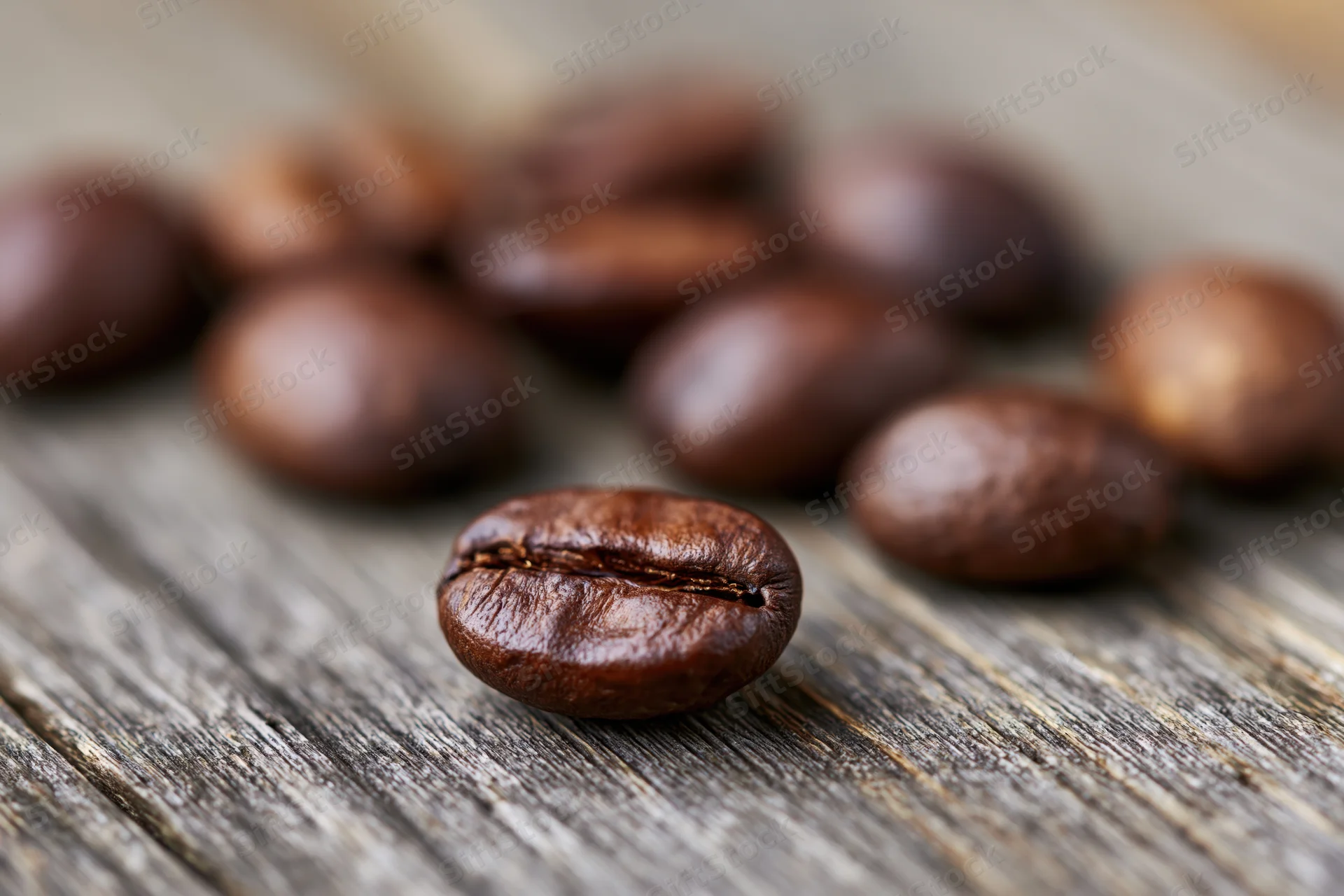 Roasted coffee beans scattered on a weathered wooden surface in close-up macro view