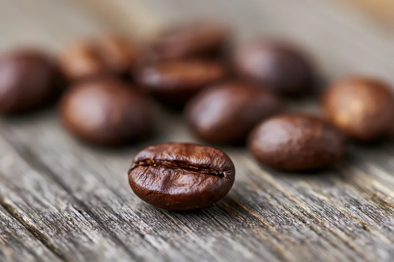 Roasted coffee beans scattered on a weathered wooden surface in close-up macro view