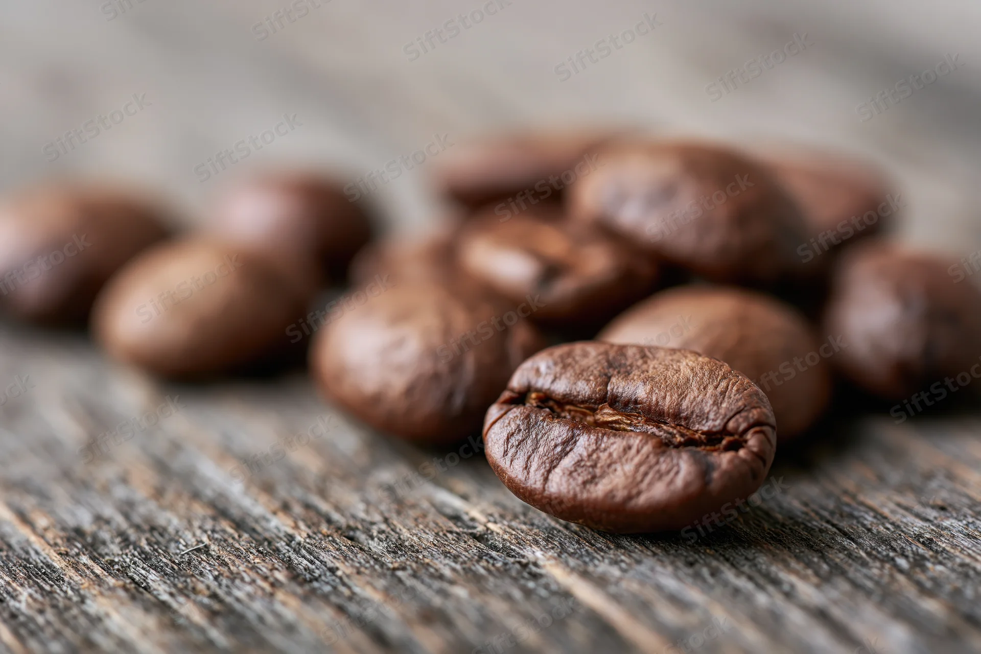 Roasted coffee beans scattered on a weathered wooden surface in close-up macro view
