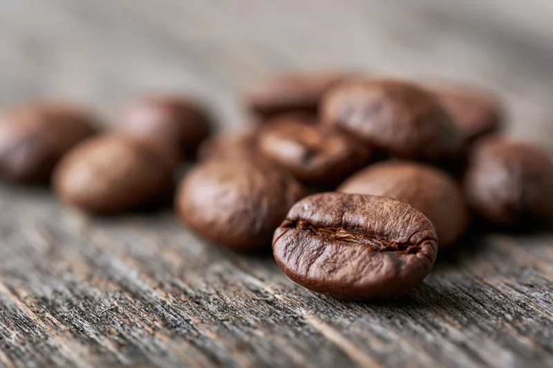 Roasted coffee beans scattered on a weathered wooden surface in close-up macro view