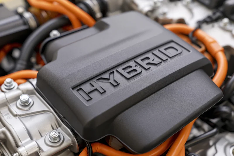 Close-up of hybrid car engine bay with matte black cover and orange cables