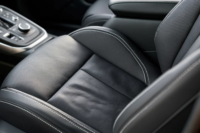 Close-up of black perforated leather driver's seat with white stitching in modern car interior