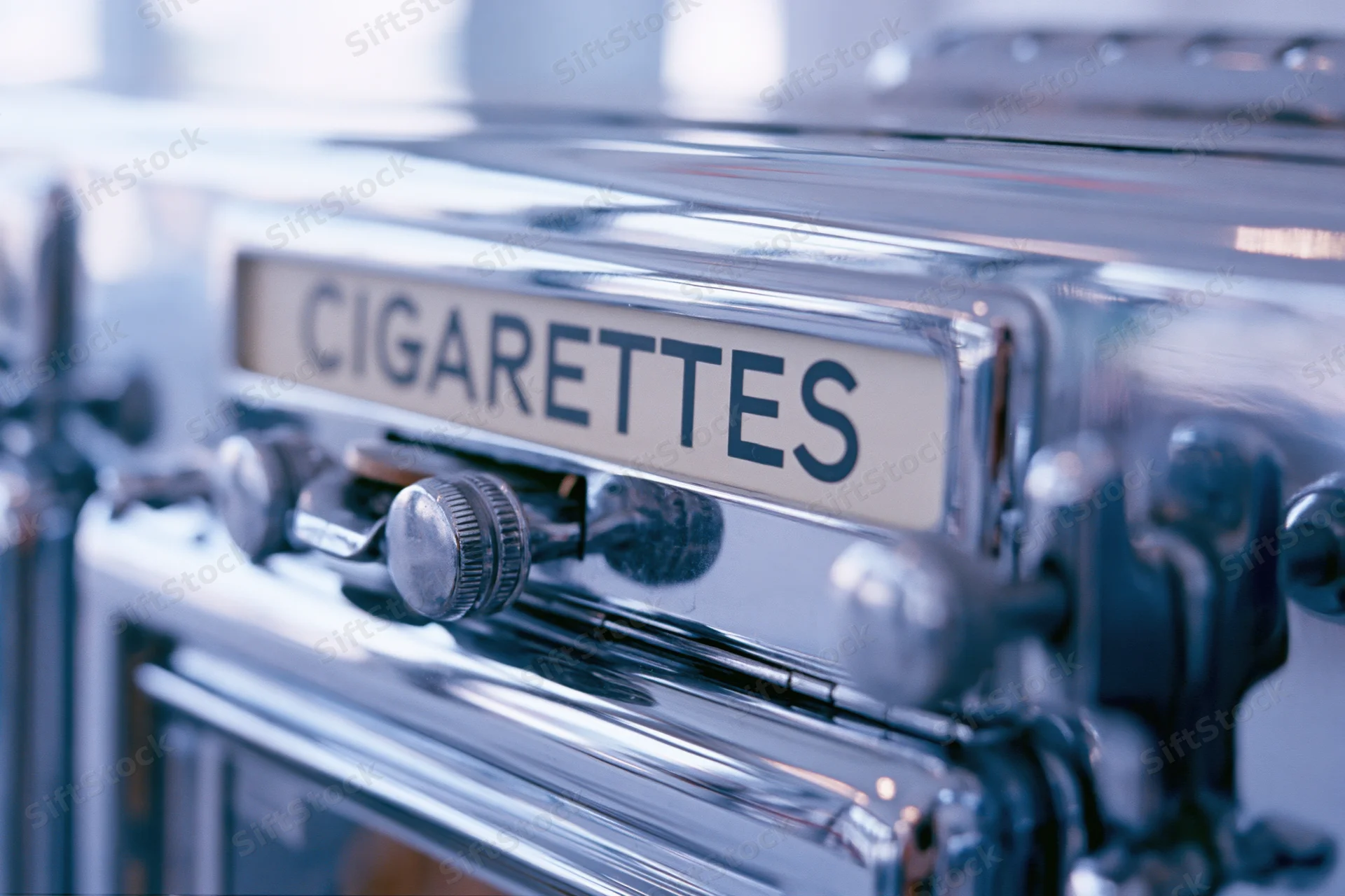 Close-up of a vintage chrome cigarette vending machine with a label and coin slot